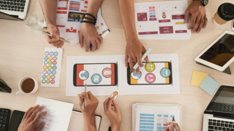 Hands of developers discussing interface of mobile app, view from above