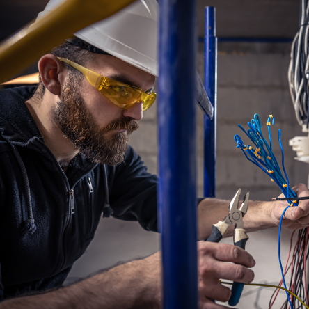 A male electrician works in a switchboard with an electrical connecting cable, connects the equipment with tools.