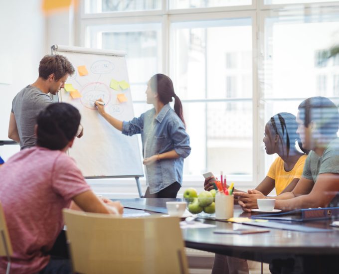 Business executives discussing with their colleagues on whiteboard during meeting at office